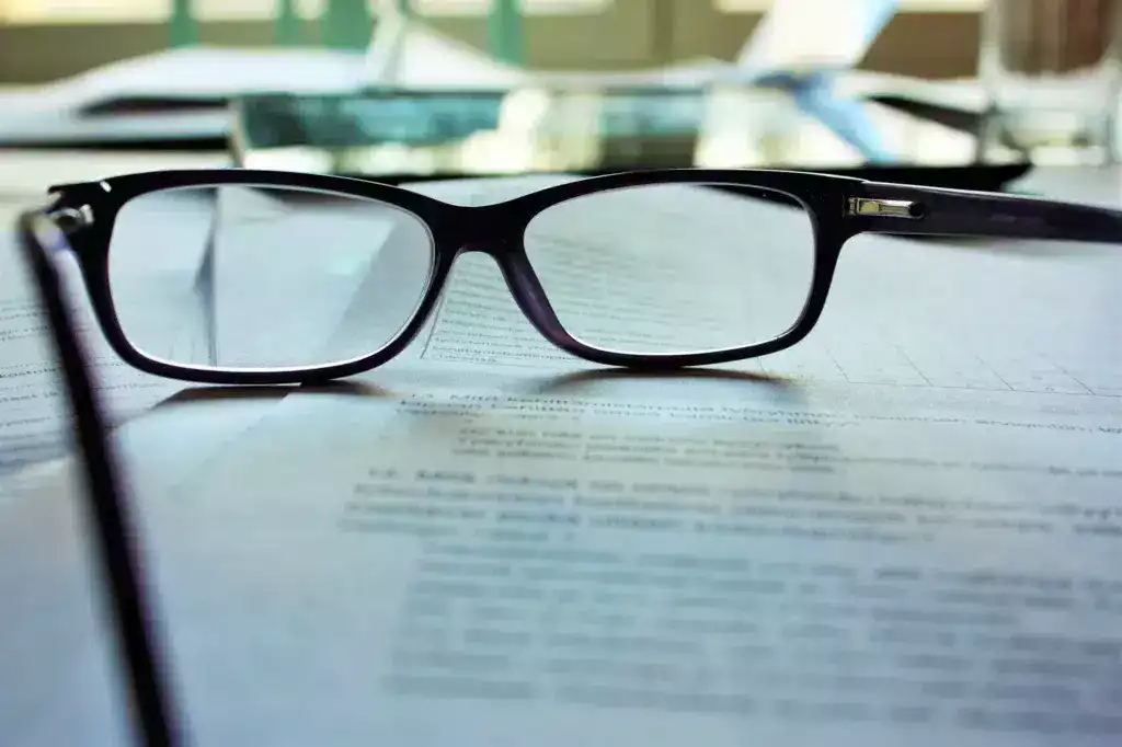משקפיים מונחים על מסמכי הכנה ל- IELTS, המייצגים אימון להשגת הסמכה ולמעבר מטרות מבחן IELTS.